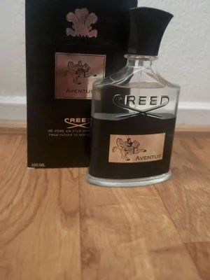Creed Aventus Eau de Parfum 100 ml - Creed Aventus är en exklusiv parfym i en elegant glasflaska med svart och silverdetaljer. Flaskan har en svart etikett med en ryttare och texten Aventus. Kommer med originalkartong och rymmer 100 ml. Doften är känd för sin fruktiga och maskulina karaktär.