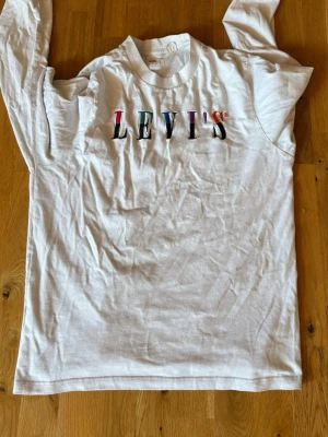 Levis tröja - Snygg vit långärmad t-shirt från Levi's med färgglatt tryck på bröstet. Tillverkad i mjuk bomull och har en klassisk rund halsringning. Perfekt för en avslappnad och trendig stil.