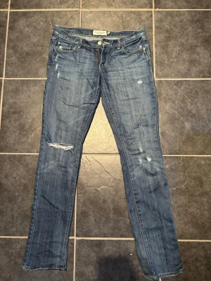 Blå jeans Abercrombie & Fitch - Säljer ett par blå jeans. Klassisk femficksmodell med dragkedja och knapp. Jeansen har en smal passform och är tillverkade i denim med lätt stretch. Är lågmidjade.