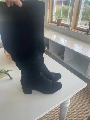 Svarta höga stövlar med klack - Säljer ett par svarta höga stövlar/boots med bred klack och rund tå. Stövlarna har dragkedja på sidan och är i ett mjukt mockaliknande material. Perfekta för att lyfta vilken outfit som helst.