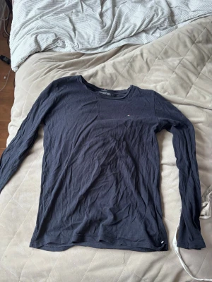 Mörkblå långärmad tröja Tommy Hilfiger - Snygg mörkblå långärmad tröja från Tommy Hilfiger i ekologisk bomull. Tröjan har en liten diskret logga på bröstet och klassisk rund halsringning. Perfekt basplagg för en clean och stilren look.