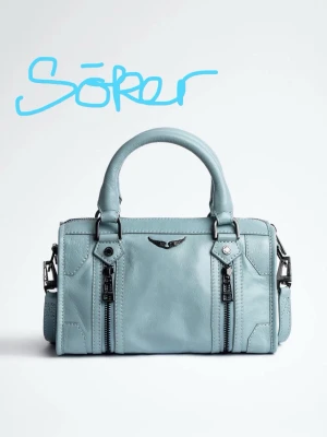 SÖKER Zadig et Voltaire Sunny i Ljusblå - Söker en ljusblå Zadig & Voltaire sunny ljusblå  handväska i cylinderformad modell med dubbla handtag och coola metalldetaljer. Väskan har två dragkedjor framtill och en liten logga i metall. Materialet ser ut som slätt konstläder och väskan har en modern vibe.