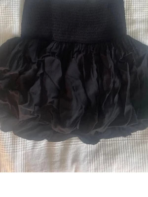 Svart bubblig kortkjol - Supersöt svart kortkjol med bubblig volym och bred, smockad midja. Kjolen har en luftig känsla och passar perfekt till en trendig och avslappnad stil. Enkel att matcha med både crop tops och oversized tröjor. Fint skick