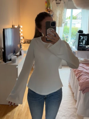 Vit topp med vida ärmar och knyt - Trendig vit topp med långa, vida ärmar och snygg knytning i ryggen från Nelly. Toppen har en clean look framtill och öppen detalj baktill som ger en unik twist. Har inte använt denna förutom vid test💕