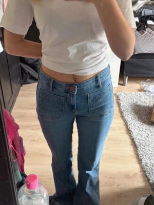 Blå bootcut jeans med fickor fram - Säljer ett par blå bootcut jeans med hög midja och raka ben. Jeansen har två stora fickor fram och två bak, samt klassisk knapp- och dragkedjestängning. Materialet är denim i bomull och de har en tidlös blå tvätt. Byxorna är knappt använda, köpte för några dagar sedan. Men säljer för att jag råka köpa fel storlek. Priset kan diskuteras. Storlek 28 i midjan och 32 i längden. 