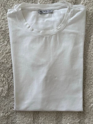 Vit basic t-shirt från Zara - En klassisk vit t-shirt från Zara med rund halsringning. Tillverkad i mjuk bomull och har en enkel, clean look som passar till allt. Perfekt basplagg för alla tillfällen.