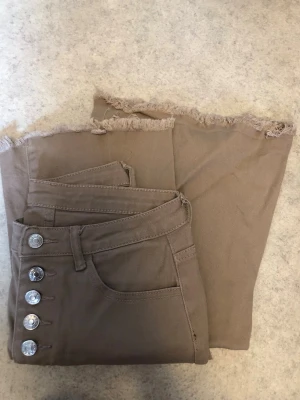 Beiga jeans med rå kant från SHEIN - Snygga beiga jeans från SHEIN med hög midja, fyra silverknappar och råa, fransiga benslut. Jeansen har klassiska fickor fram och bak och är tillverkade i en stretchig bomullsblandning. Perfekta för en trendig och avslappnad look.