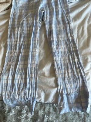 Ljusblå rutiga pyjamasbyxor - Mysiga pyjamasbyxor i ljusblått och vitt rutmönster. Byxorna har rak passform och resår i midjan för extra komfort. Perfekta för slappa dagar hemma eller en god natts sömn. Materialet känns mjukt och lätt mot huden.