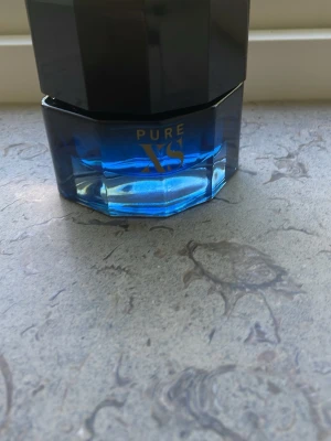 PURE XS Eau de Toilette 50ml - En snygg parfymflaska med blått glas och svart lock. PURE XS är en Eau de Toilette för honom, 50 ml, med elegant och modern design. Flaskan har en oktagonal form och guldtext på framsidan. Perfekt för dig som gillar stilrena och maskulina dofter. Hela flaskan är full 