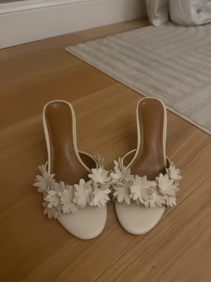 Vita pumps med blommor och klack - Säljer ett par vita pumps med öppen tå och låg klack. I storlek 39 från NAKD aldrig använda. Fina och prisvärda klackar då jag köpte dem för 900. Jätte sköna att gå i också❤️