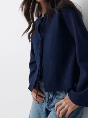 Mörkblå stickad tröja med knytning - Trendig mörkblå stickad tröja från Gina Tricot med tre knytningar framtill. Tröjan har rund halsringning, långa ärmar och en rak passform. Perfekt att styla med jeans för en cool look.
