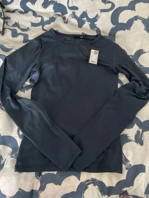 Mörkblå långärmad topp - Snygg mörkblå långärmad topp med rund halsringning och tight passform. Tillverkad i ett stretchigt syntetmaterial som sitter skönt mot kroppen. Perfekt att styla med jeans eller kjol för en clean look. 
