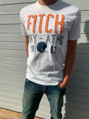 Abercrombie vintage T-shirt - Snygg vintage t-shirt av märket Abercrombie & Fitch med deras klassiska tryck i form av varumärkesnamnet på bröstet. Tröjan är storlek M och true to size, om något så är den lite liten i storleken. Modellen är 178 cm lång och väger 65 kg. Notera även den lilla fläcken på mitten av framsidan (se bilder)   Skriv vid frågor och funderingar!