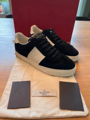 Svarta och vita sneakers från Valentino - Snygga sneakers från Valentino i svart mocka med vita detaljer och vit sula. Skorna har svarta skosnören, vit panel på sidan och vit insida. Klassisk låg modell med diskret logga på plösen. Perfekta för dig som gillar stilrena och exklusiva sneakers. Storlek 36,5 ( inte mina bilder tjejen jag köpte de utav! ) 