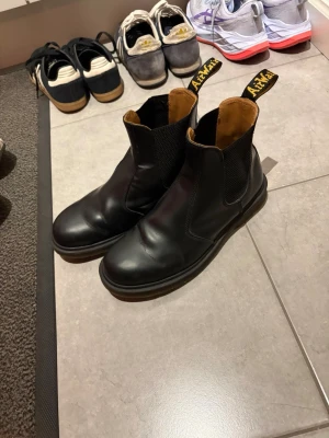 Chelsea boots Dr. Martens 2976 - Säljer ett par klassiska svarta Chelsea boots från Dr. Martens i slätt läder. Skorna har elastiska paneler på sidorna och den ikoniska gula AirWair-dragfliken bak. Köpta på Zalando på rea 2023 men inte använda så mycket som man ser på yttersulan. Hämtas i bromma eller fraktas men har slängt orginal skolådan så i en annan låda