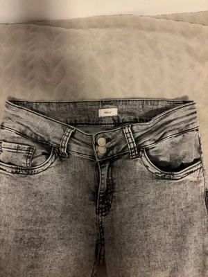 Gråa bootcut jeans från Nelly - Säljer ett par gråa bootcut jeans från Nelly med tvättad look och dubbla knappar i midjan. Jeansen har klassiska fem fickor och snygga detaljer på bakfickorna. Perfekta för dig som gillar en trendig och avslappnad stil.
