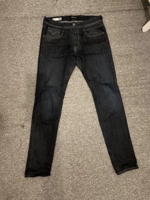 Mörkblå slim jeans med kontrastsömmar - Säljer ett par mörkblå jeans i slim fit med klassiska kontrastsömmar och femficksmodell. Jeansen har en enkel design med raka ben och subtila detaljer på bakfickorna. Perfekta för dig som gillar en clean och stilren look.