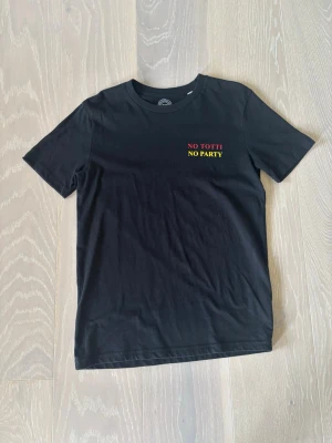 Svart t-shirt med tryck 'NO TOTTI NO PARTY' - Svart t-shirt i bomull med trycket 'NO TOTTI NO PARTY' i rött och gult på bröstet. Klassisk rund hals och korta ärmar. Perfekt för dig som gillar fotboll och vill ha en enkel men snygg statement-tee. Vid intresse eller frågor är det bara att höra av sig 