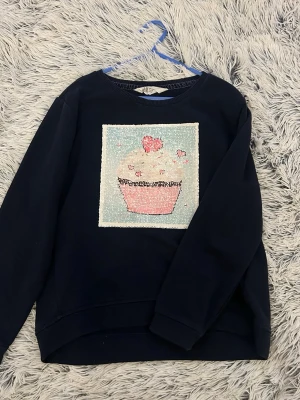 Mörkblå sweatshirt med paljettmotiv - Cool mörkblå sweatshirt med paljettmotiv som kan vändas – ena sidan visar en cupcake och den andra en enhörning. Tröjan har rund hals och långa ärmar. Perfekt för dig som gillar att byta stil snabbt och vill ha något unikt i garderoben. Från h&m i storlek 134/140 💖 