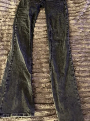 Grå bootcut jeans med tvättad look - Säljer ett par grå bootcut jeans med tvättad vintage-look. Jeansen har klassisk femficksmodell, hög midja och vida ben. Materialet är denim i bomull och de har snygga sömdetaljer. Perfekta för dig som gillar retrostil och vill ha ett par statement-jeans.