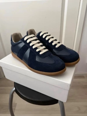 Marinblå sneakers med mockadetaljer - Snygga marinblå sneakers med både mocka och släta paneler, vita snören och beige innersula. Yttersulan är i gummi med klassisk brun färg. Perfekta för dig som gillar stilrena och tidlösa sneakers med en sportig touch.