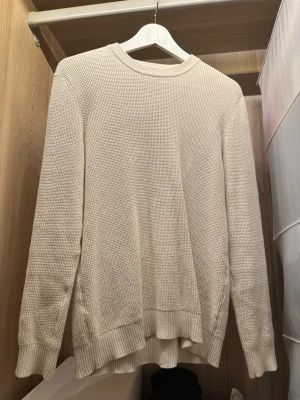 Beige stickad tröja med rund hals - En stilren beige stickad tröja med rund halsringning och långa ärmar. Tröjan har en grovstickad struktur och ribbade muddar vid ärmslut och nederkant. Perfekt för lager på lager och enkel att matcha med olika outfits.
