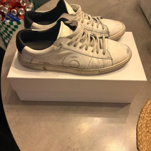 Vita oliver cabell sneakers  - Snygga vita sneakers med svart detalj på hälen och vita skosnören. Skorna har en låg profil och rundad tå, samt diskreta sömmar och mönster på sidan. Passar perfekt till streetwear och casual outfits. Storlek 43. De är använda i ungefär 6 månader och är i bra skick.