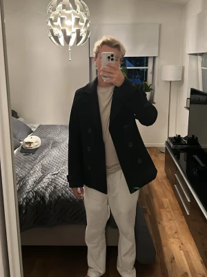 Svart skepparkavaj med bred krage - Stilren svart skepparkavaj med dubbelknäppning och bred krage. Klassisk modell som ger en snygg siluett och passar perfekt till både jeans och chinos. Jackan har två rader med knappar framtill och är tillverkad i ett kraftigare tyg.