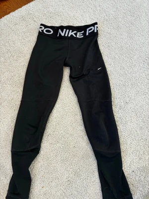 Svarta Nike Pro leggings - Säljer ett par svarta Nike Pro leggings med bred resår i midjan där det står 'NIKE PRO' i vitt. Tight passform och stretchigt material som passar perfekt till träning eller chill. Klassisk sportig look och bekväma att bära hela dagen.