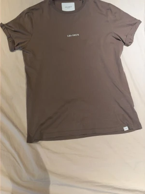 Brun t-shirt från Les Deux - Snygg brun t-shirt från Les Deux med minimalistiskt tryck på bröstet. Klassisk rund halsringning och diskret etikett nertill. Tillverkad i mjuk bomull som känns skön mot huden. Perfekt för en clean och stilren look.