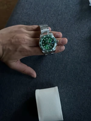 Grön och silverfärgad klocka - Stilren klocka med grön urtavla och silverfärgat armband i metall. Klockan har tydliga markeringar, datumfönster och vridbar bezel. Perfekt accessoar för dig som vill sticka ut med en cool färgkombination. 