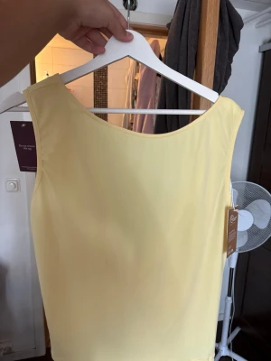 Gul ärmlös croppad topp med knyt - Snygg gul ärmlös topp med croppad passform. Toppen har en djup v-ringning i ryggen och är tillverkad i ett mjukt, lätt material som passar perfekt till sommaren.