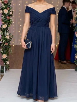 Marinblå offshoulder långklänning - Elegant marinblå långklänning med offshoulder och omlott överdel. Klänningen har ett flytande, svepande fall och markerad midja. Perfekt för bal eller festliga tillfällen eller prom. Tillverkad i ett lätt, mjukt material som ger en lyxig känsla.