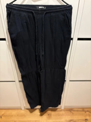 Svarta linnebyxor från Gina Tricot - Snygga svarta linnebyxor från Gina Tricot i storlek XS. Byxorna har resår i midjan med dragsko och är tillverkade i ett luftigt linnematerial. Perfekta för en avslappnad och trendig look. De har hängt på en galge därför dom har en liten kant. 