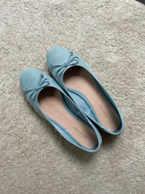 Ljusblå ballerinaskor med rosett - Snygga ljusblå ballerinaskor från Primark med en söt rosett framtill. Skorna har en mjuk ovandel i mockaimitation och en klassisk rund tå. Perfekta för dig som gillar stilrena och bekväma skor i en fräsch färg.