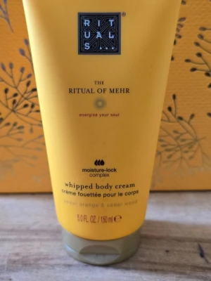 Rituals The Ritual of Mehr body cream - Lyxig whipped body cream från Rituals i serien The Ritual of Mehr. Kommer i en gul tub på 150 ml och innehåller doft av söt apelsin och cederträ. Innehåller moisture-lock complex för extra återfuktning. Perfekt för dig som vill ha en fräsch och energigivande hudvård.