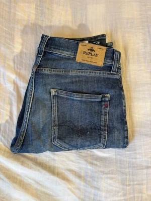 Blå jeans från Replay Wallys - Säljer ett par klassiska blå jeans från Replay med snygg tvätt och raka ben. Jeansen har fem fickor, tydliga sömmar och en läderpatch med Replay-loggan bak i midjan. Perfekta för dig som gillar en tidlös och avslappnad stil. Dessa är ett par Wally
