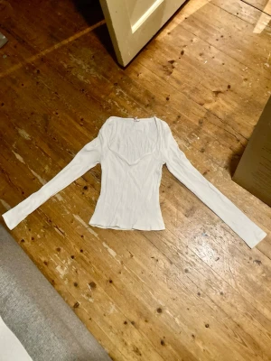 Vit ribbad långärmad topp, från Nelly - Säljer en vit ribbad långärmad topp med v-ringad hals, från Nelly i storlek Medium. Den har en figurnära passform och är tillverkad i ett mjukt material som sitter snyggt på kroppen. Säljes pga för liten🤗