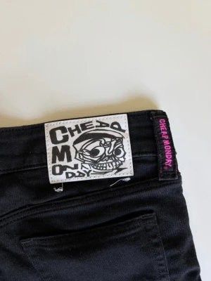 Svarta Cheap Monday jeans - Snygga svarta jeans från Cheap Monday med klassisk döskalle-logga bak och raka bakfickor. Jeansen är bootcut och är tillverkade i ett stretchigt material för extra komfort. Perfekta för dig som gillar en clean och stilren look. 