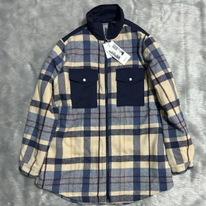 Rutig overshirt från Fransa - Overshirt i beige, blått och brunt rutmönster från Fransa. Två stora bröstfickor i mörkblått tyg med lock och knapp. Dragkedja framtill och hög krage. Perfekt lager på lager-plagg med avslappnad passform och mjukt material. Inköpt för 1000kr