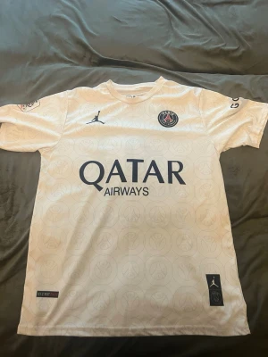 PSG Messi matchtröja vit - Säljer en vit PSG matchtröja med Messi och nummer 30 på ryggen. Tröjan har mörkblå detaljer, Qatar Airways-tryck på bröstet och PSG-logga samt Jordan-logga. Tillverkad i lätt och ventilerande material, perfekt för fotboll eller träning. Passar även för mindre storlekar som L