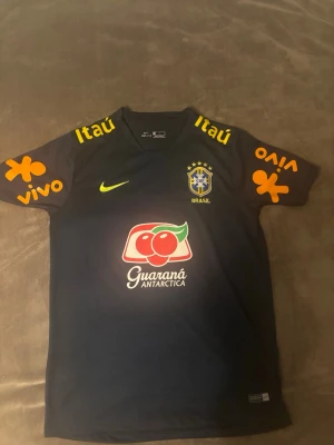  Brasilien tröja i storlek S - Säljer en svart tränings t-shirt från Nike med Brasilien-logga på bröstet och flera färgglada sponsorloggor i gult, orange och rött. Tillverkad i Dri-Fit material som andas, perfekt för fotbollsträning eller gymmet.