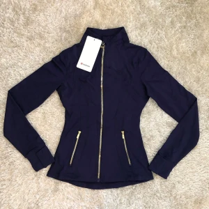 Lululemon Define Jacket Luon – Mörkblå, storlek 2 - Helt ny med etiketter. Mjuk, stretchig och figurnära modell i Luon-material med guldfärgad dragkedja. Färg: Mörkblå Storlek: 2 Helt ny med etiketter Hör av dig vid intresse!