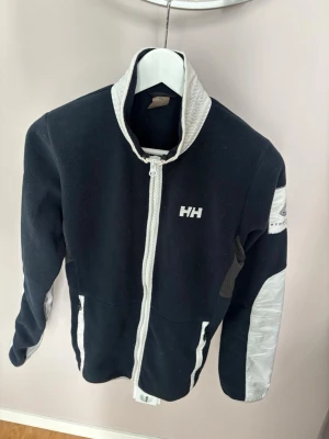 Jättefin ursnygg Helly Hansen fleece jacka M - Supersnygg populär eftertraktad Helly Hansen fleece jacka XS säljes. Grym passform perfekt nu till vintern och tveka inte vid minsta fråga. Jättefint utmärkt skick och blått fint material som vaddering så varm och skön!