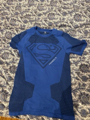 Blå Superman t-shirt från YoungLA - Snygg blå t-shirt från YoungLA med stort Superman-tryck på bröstet och coola mönstrade detaljer på axlar och sidor. Perfekt för dig som vill sticka ut med en superhjälte-look. Rund hals och korta ärmar för en avslappnad vibe.