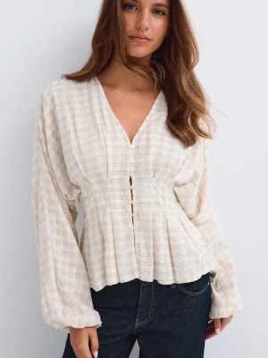 Beige rutig blus - Snygg beige blus med diskret rutmönster och v-ringning. Blusen har långa ärmar, knappar framtill och lätt utsvängd midja som ger en feminin siluett. Tillverkad i ett mjukt, luftigt tyg som känns skönt mot huden.