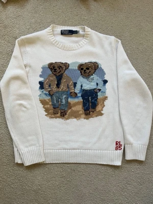  Polo Ralph Lauren ”Ralph & Ricky”  - Vit stickad tröja från Polo Ralph Lauren med ikoniskt björnmotiv framtill. Säljs ej mer! Tröjan har rund halsringning, ribbade muddar och RL85-brodyr nertill. Motivet visar två björnar i coola outfits, en med solglasögon och klocka. Perfekt för dig som gillar statement-plagg. Nypris 450€-600€. Skickar till sverige🇸🇪