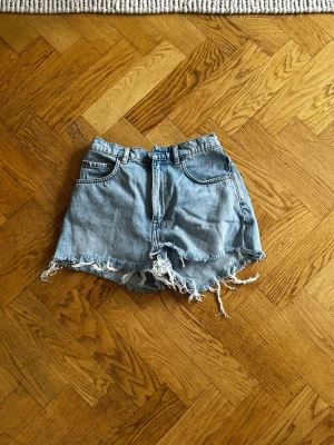 Ljusblå denimshorts från & Other Stories - Säljer ett par ljusblå denimshorts från & Other Stories med råa, fransiga kanter och klassisk femficksdesign. Shortsen har hög midja och är perfekta för varma dagar. Styla med din favorit-topp för en chill look.