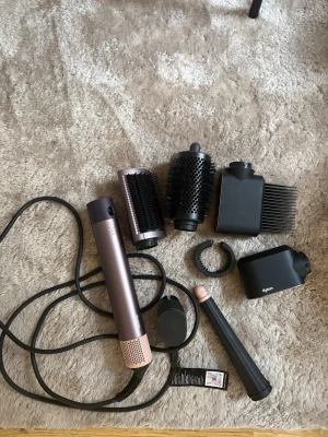 Dyson Airwrap med flera tillbehör - Säljer en Dyson Airwrap i metalliclila med flera stylingtillbehör som rundborste, volymborste, diffuser, kam och locktillbehör. Perfekt för att skapa olika frisyrer och looks. Sladd och förvaringsväska ingår. Modern design och hög kvalitet. Priset kan diskuteras vid snabb affär!