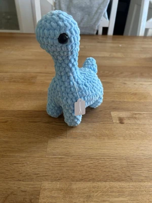 Virkad blå dinosaurie  - Söt handgjord dinosaurie i mjukt, blått garn med stora svarta säkerhetsögon. Perfekt som dekoration eller gosedjur. Den har lång hals, liten svans. Passar både som present eller till samlingen.